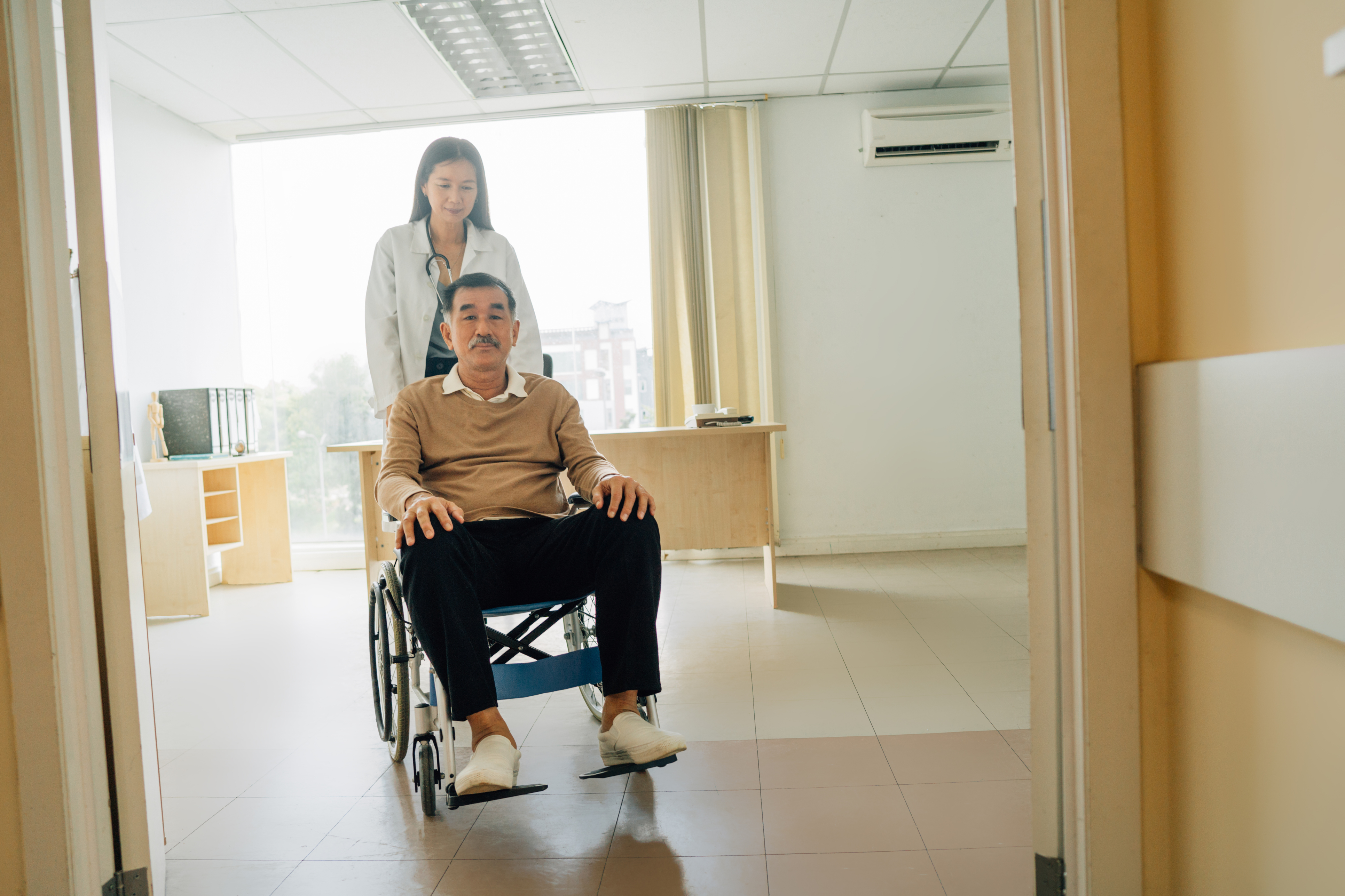 Medical assistant pushing man in wheelchair iStock-1391165723 Medical assistant pushing man in wheelchair